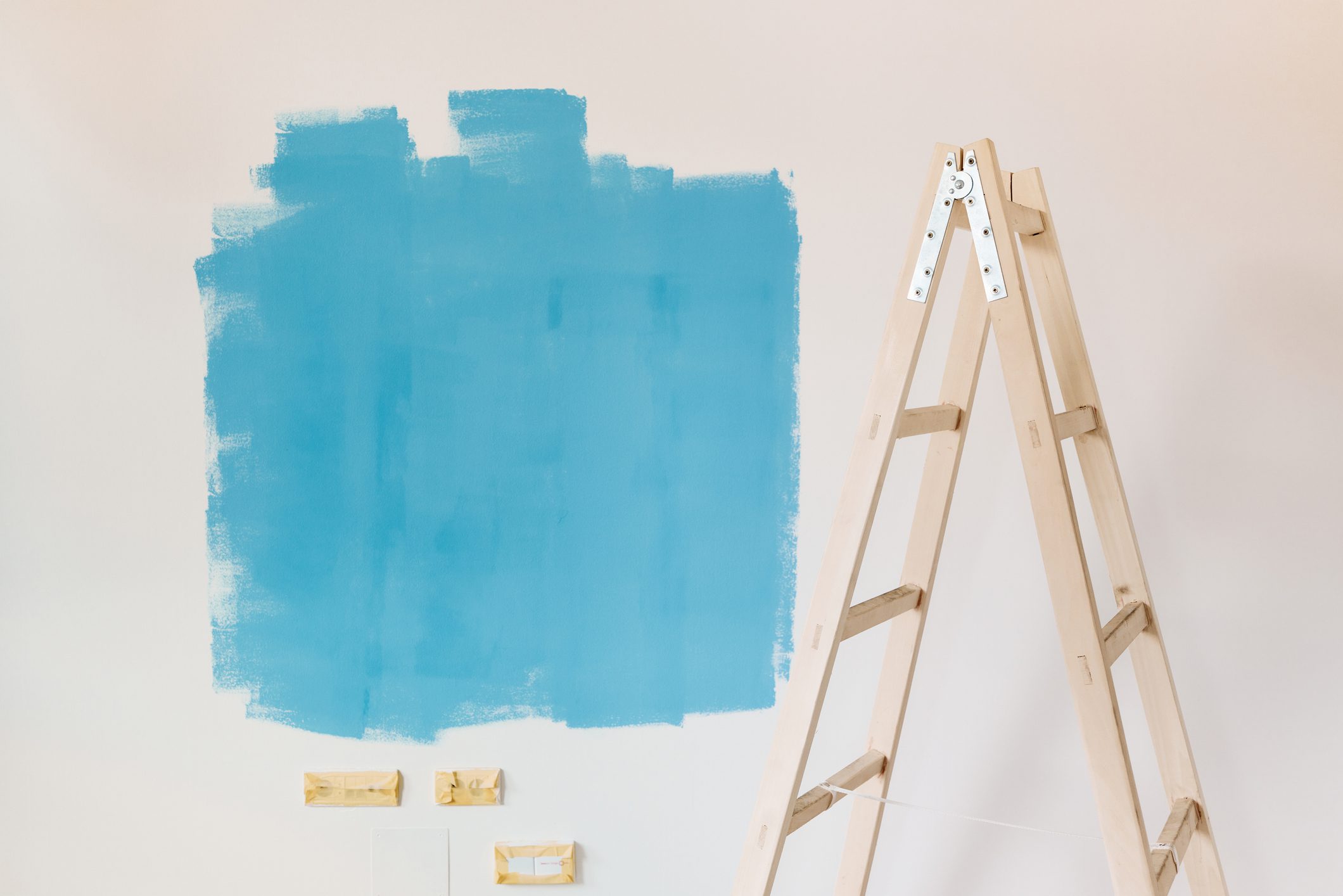 A partially painted wall in blue with a ladder nearby.