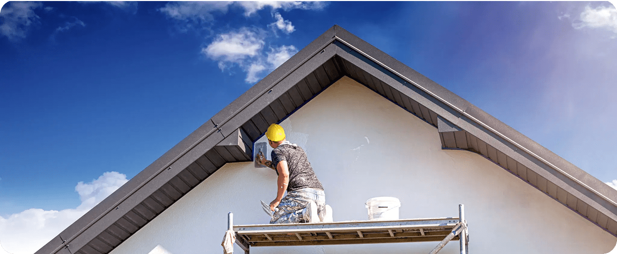 Worker painting house exterior on scaffold
